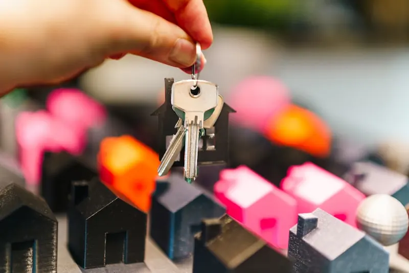 A hand holding a set of house keys above small model houses