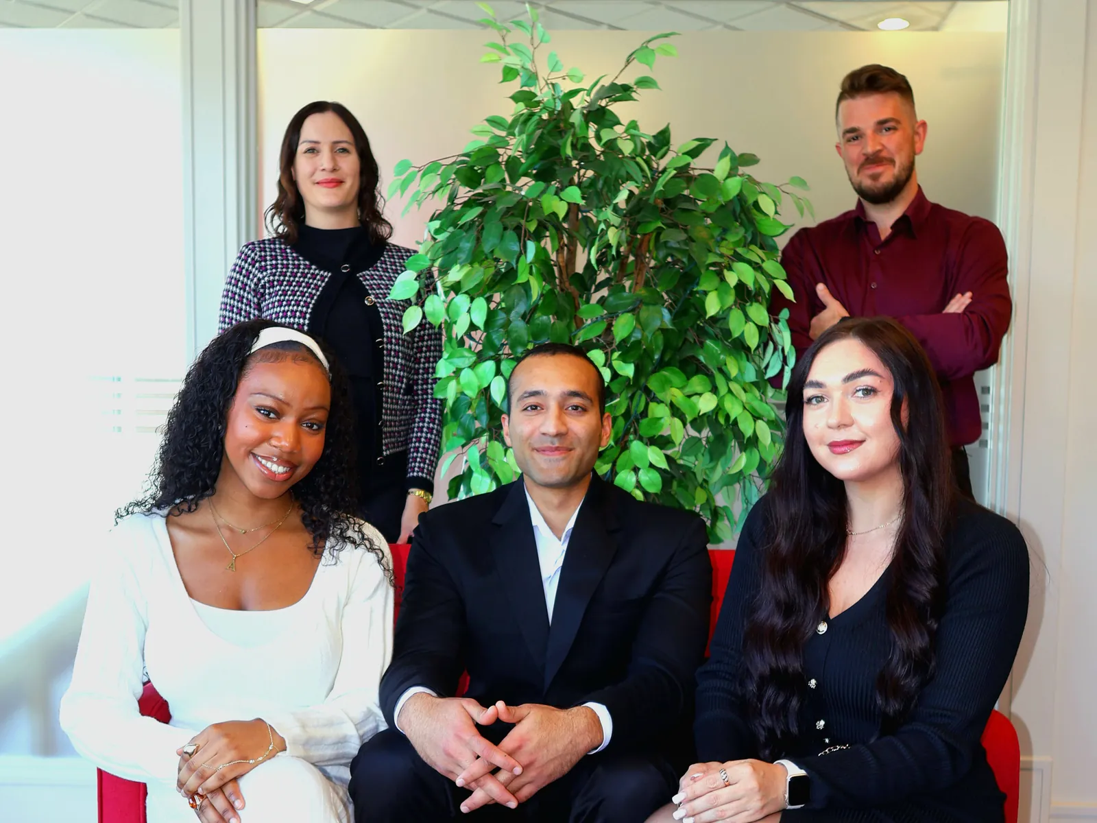 The L|S Real Estate Group team at the office: Natasha Sutherland and Tony Lucas standing behind Adaora Awolesi, Bineet Kalra and Lana Lesiuk, seated on a red sofa